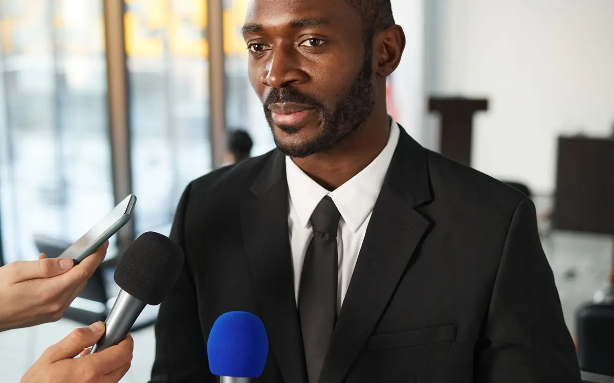 Journalists holding microphones around an interviewee at a press event